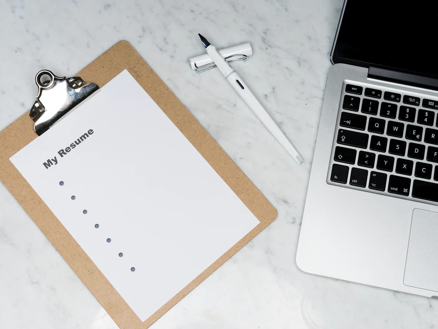 Clipboard with a checklist beside an open laptop on a marble desk
