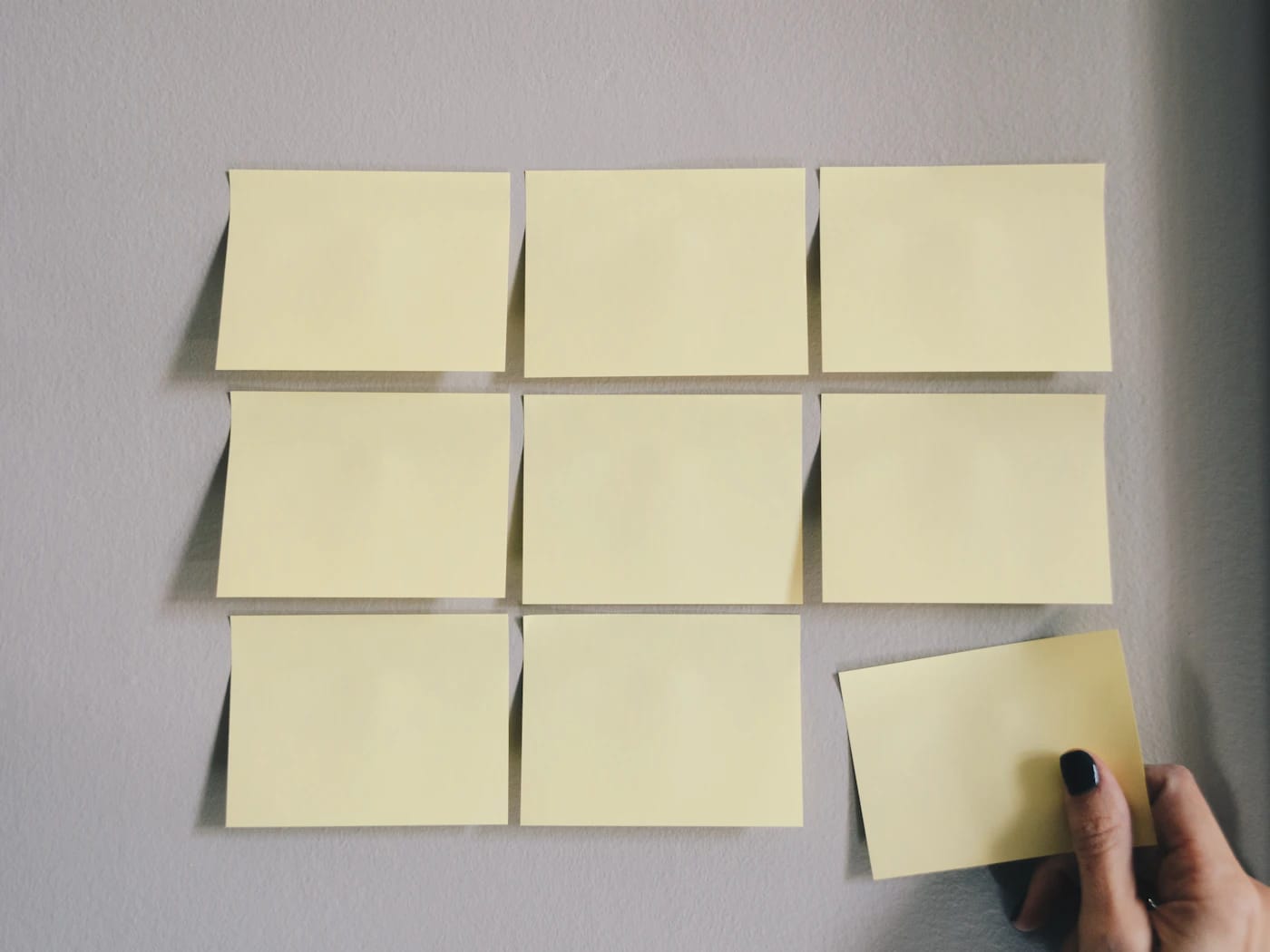 Hand placing sticky notes in a grid on a wall during a planning session