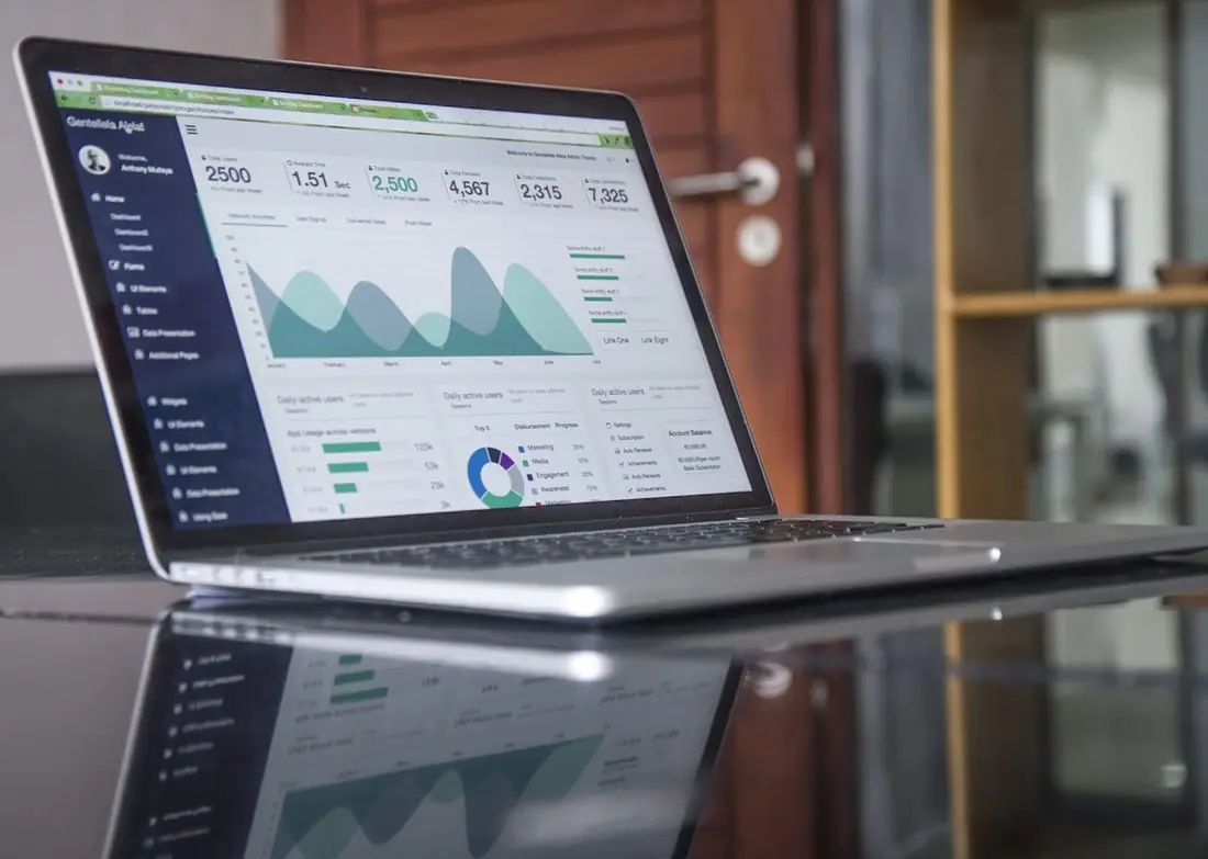 Laptop on a reflective desk displaying an analytics dashboard with area charts