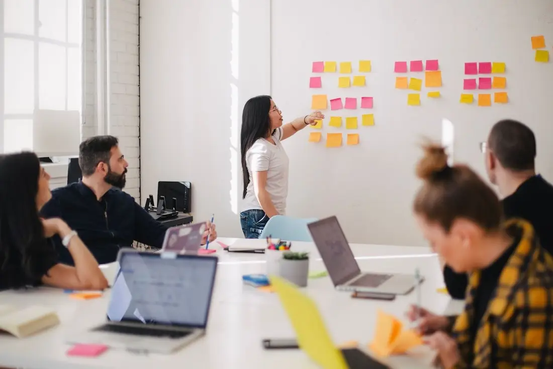 Team seated around a meeting table while a colleague arranges sticky notes on a whiteboard